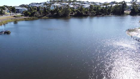 Drone-Volando-Sobre-Un-Lago-Artificial-Hacia-Un-Suburbio-Australiano-Con-Grandes-Casas-Familiares