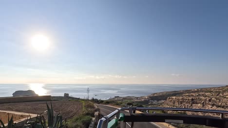 Panoramic-view-from-the-top-deck-of-an-open-touristic-bus-in-Gozo,-Malta,-showcasing-a-sunny-seaside-road