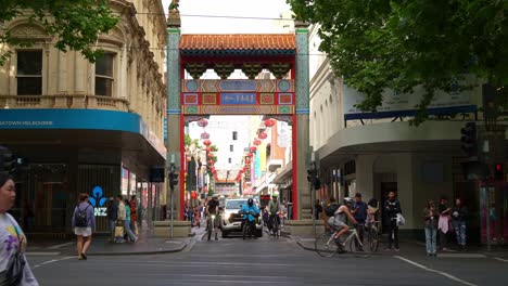 Bustling-downtown-Melbourne-city-featuring-iconic-landmark-Chinatown-with-pedestrians-crossing-on-the-crosswalk-and-vehicle-traffic-along-Little-Bourke-street,-captured-in-slow-motion-shot