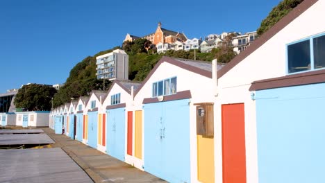 A-row-of-iconic-colourful-boat-sheds-in-Chaffer-Marina-alongside-waterfront-of-Oriental-Parade-in-Wellington,-New-Zealand-Aotearoa