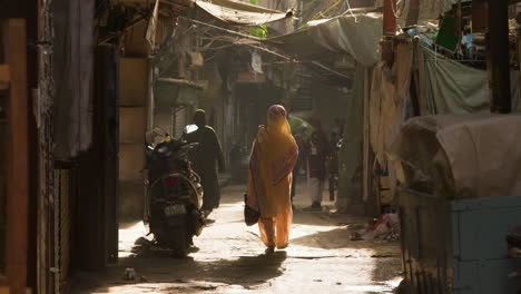 Woman-walks-down-sunlit-alleyway-in-Old-Delhi,-India