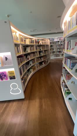 POV-Walking-Inside-The-Modern-Library-Between-Bookshelves-Along-The-Aisle