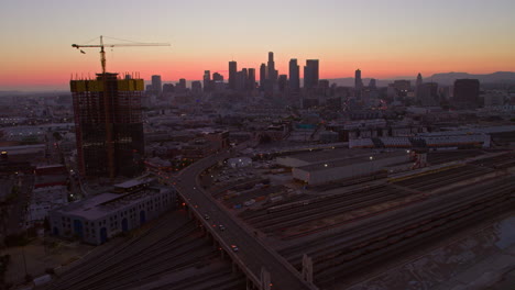 Aerial-of-downtown-Los-Angeles-overlooking-its-central-railway-station-against-a-backdrop-of-city-skyline-bathed-in-evening-hues,-showcasing-the-city's-vibrant-urban-connectivity