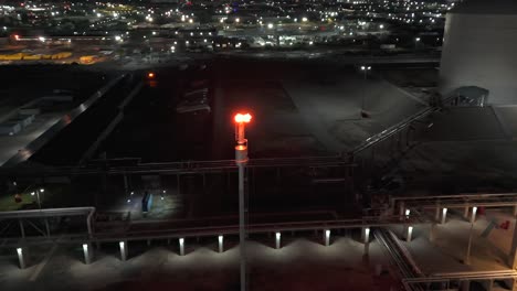 An-aerial-view-of-an-industrial-plant-with-white-tanks-and-pipes-with-a-tall-pipe-with-flames-at-the-top