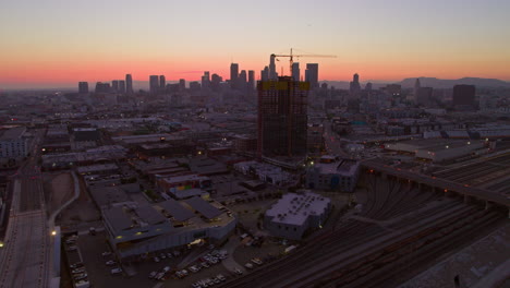 Aerial-perspective-of-downtown-Los-Angeles,-overlooking-the-central-railway-station-with-a-backdrop-of-the-city-skyline-bathed-in-evening-hues,-capturing-the-essence-of-urban-connectivity-of-the-city