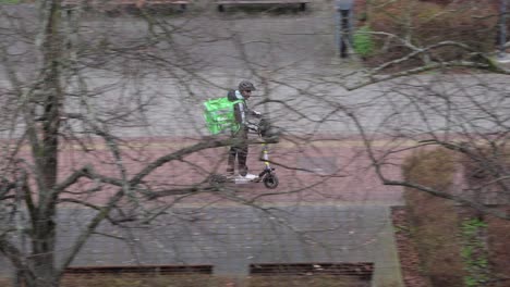 Man-on-electric-scooter-delivering-food-for-Bolt-Food-service-in-Ostrava,-panning-shot