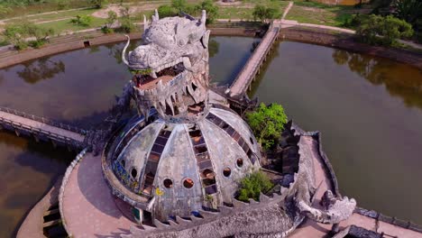 Aerial-view-of-an-abandoned-water-park-in-Hue,-Vietnam,-featuring-a-dragon-shaped-building-surrounded-by-water-and-lush-greenery