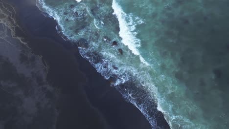 Aerial-tops-down-blue-waves-reaching-black-sand-volcanic-beach-slow-meditative-natural-environment