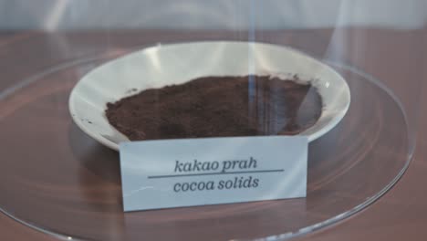 Primer-Plano-De-Una-Exhibición-Que-Presenta-Un-Tazón-De-Sólidos-De-Cacao-Bajo-Una-Cúpula-De-Vidrio-En-El-Museo-Del-Chocolate-En-Zagreb,-Croacia