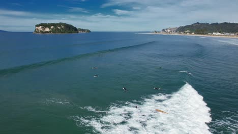 Surfers-Riding-Waves-At-Whangamata-Beach-In-Coromandel,-New-Zealand---Aerial-Drone-Shot