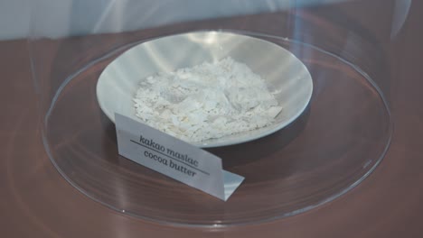 Close-up-of-a-display-featuring-a-bowl-of-cocoa-butter-flakes-under-a-glass-dome-in-the-Chocolate-Museum-in-Zagreb,-Croatia