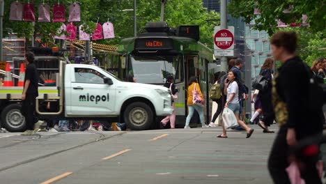 Tram-stop-at-the-traffic-light-on-Swanston-Street-in-Melbourne's-bustling-central-business-district,-as-pedestrians-cross-at-the-crosswalks,-showcasing-the-hustle-and-bustle-of-urban-lifestyle