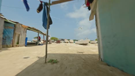 Schnelle-FPV-Drohne-Geschossen-Durch-Ein-Kleines-Fischerdorf-In-Richtung-Einer-Bucht-Mit-Kitesurfer-In-Los-Roques,-Venezuela