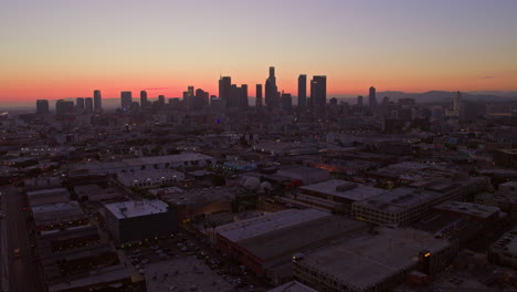 From-an-aerial-view-above-downtown-Los-Angeles,-the-central-railway-station-stands-against-the-backdrop-of-the-city-skyline-glowing-in-the-evening-light,-highlighting-the-city's-urban-connectivity