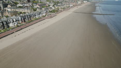 Aufschlussreiche-Luftaufnahme-Einer-Küstenstadt-In-Schottland-Mit-Reihenhäusern-Entlang-Eines-Langen-Strandes-Bei-Ebbe