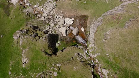 Tiered-mountain-waterfall-cascades-down-rugged-cliffs-on-a-sunny-day,-top-drone-view