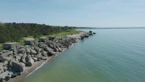 Beautiful-aerial-establishing-view-of-Karosta-concrete-coast-fortification-ruins,-calm-Baltic-sea,-sunny-summer-day,-wide-drone-shot-moving-forward