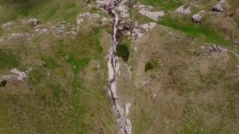 An-Einem-Sonnigen-Tag-Stürzt-Ein-Bergwasserfall-Schroffe-Klippen-Hinab,-Drohnenansicht-Von-Oben