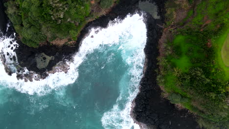 Aerial-View-Down-of-Waves-Splashing-Between-Cliffs-of-Princeville,-HI