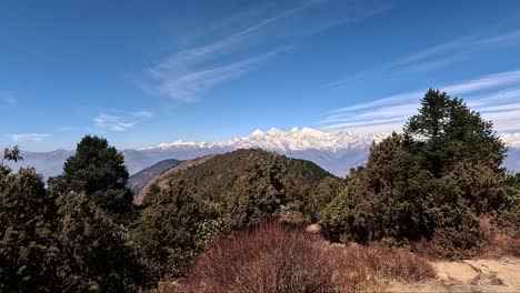 High-altitude-panorama-with-pine-forests,-snowy-Ganesh-Himaly-mountain-range-with-a-hut-in-the-foreground