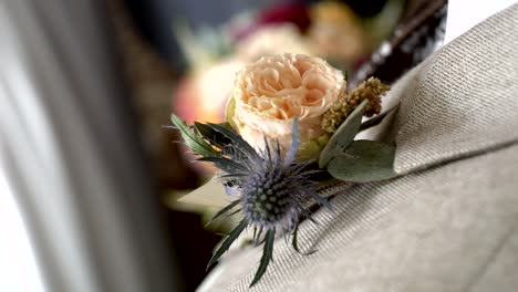 Boutonniere---a-tea-colored-flower-with-green-leaves,-pinned-to-the-lapel-of-a-jacket