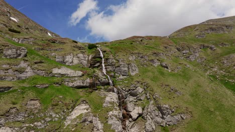 An-Einem-Sonnigen-Tag-Stürzt-Ein-Mehrstufiger-Bergwasserfall-Schroffe-Klippen-Hinab,-Drohnen-Kamerafahrt