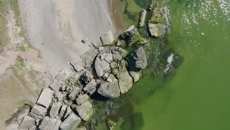 Beautiful-aerial-revealing-view-of-Karosta-concrete-coast-fortification-ruins,-calm-Baltic-sea,-sunny-summer-day,-descending-birdseye-drone-orbit-shot