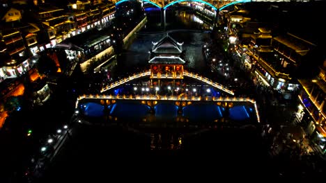 Aerial-night-reveal-shot-of-illuminated-Snow-Bridge-and-Tuo-Jiang,-Fenghuang