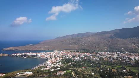 An-aerial-view-of-a-coastal-town-with-white-houses-and-red-roofs,-set-against-rolling-hills-and-blue-sea,-timelapse