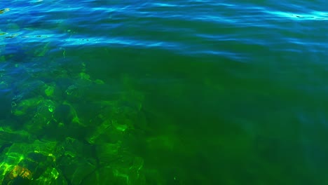 Rocky-seabed-visible-through-crystal-clear-turquoise-coastal-waters,-with-the-reflection-of-the-blue-sky-on-the-surface