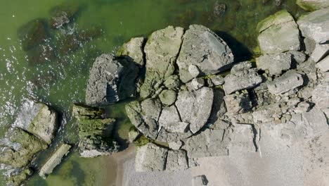 Beautiful-aerial-establishing-view-of-Karosta-concrete-coast-fortification-ruins,-calm-Baltic-sea,-sunny-summer-day,-ascending-birdseye-drone-orbit-shot