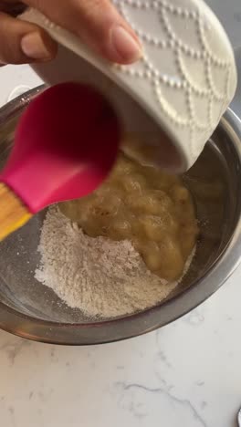 Vertical-video-of-mashed-bananas-into-a-bowl-of-flour-making-banana-donuts