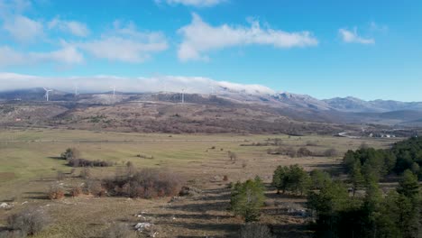 Wunderschöne-Luftaufnahme-Der-Kroatischen-Landschaft-Mit-Windturbinen,-Die-Im-Hintergrund-Erneuerbare-Energie-Erzeugen,-Und-Einer-Leeren-Straße-In-Der-Region-Lika-In-Kroatien,-Europa