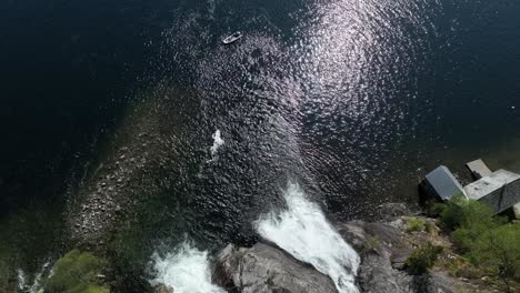 Rising-aerial-view-tilting-down,-revealing-tourists-in-a-rib-boat-at-Tysseknappen-Waterfalls-in-Norway