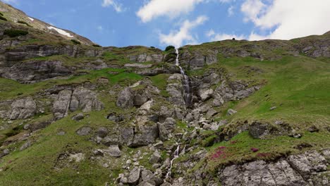 Tiered-mountain-waterfall-cascades-down-rugged-cliffs-on-a-sunny-day,-static-shot