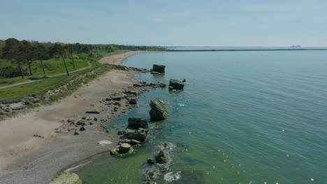 Beautiful-aerial-establishing-view-of-Karosta-concrete-coast-fortification-ruins,-calm-Baltic-sea,-sunny-summer-day,-birdseye-drone-shot-moving-forward