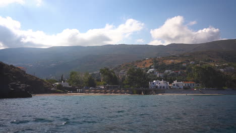 Beautiful-beach-with-sunbathers-and-umbrellas,-surrounded-by-lush-greenery-and-hills,-against-a-clear-blue-sky