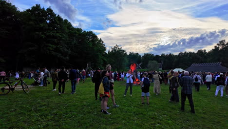 People-attending-the-Estonian-Open-Air-Museum-near-Tallinn,-gathered-around-the-bonfire,-slow-dolly-wide-angle-shot