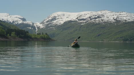 Kayaker-paddling-on-a-serene-fjord-with-snowy-mountains-in-Røldal,-Norway