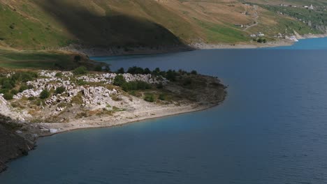 Aerial-view-of-Mont-Cenis-Lake,-showcasing-the-tranquil-blue-water-and-the-surrounding-rugged-landscape