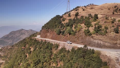 SUV-Blanco-Conduciendo-Por-Una-Carretera-Sinuosa-A-Través-De-Terreno-Montañoso,-Coche-Conduciendo-Por-Un-Empinado-Paso-De-Montaña-Rodeado-De-Escasa-Vegetación