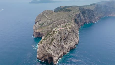 Aerial-view-of-lighthouse-tower-on-long-headland-stretch-into-sea,-Mallorca