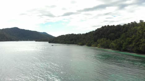 Aerial-view-of-the-lush-coastline-and-turquoise-waters-surrounding-Kri-Island-in-Raja-Ampat,-Indonesia