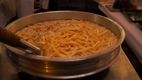 From-above-of-crop-anonymous-chef-making-French-fries-into-deep-fried-basket-in-boiling-oil-while-working-in-light-kitchen