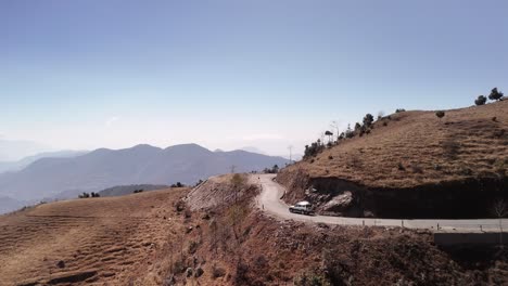 Reise-Durch-Die-Trockenen-Berge,-Einsames-Weißes-Fahrzeug-Navigiert-Serpentinenstraße-Durch-Raue,-Abgelegene,-Trockene-Berglandschaft,-Weißer-Geländewagen