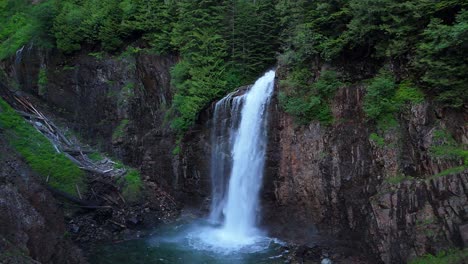 Scenic-orbital-shot-of-hidden-waterfall-cascading-down-a-cliff-side-in-Evergreen-Forest-in-the-Pacific-Northwest