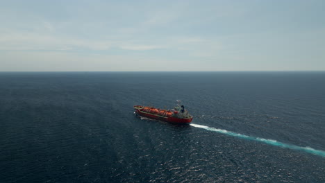 Red-tanker-ship-cruising-full-speed-in-blue-ocean,-aerial-arc-view