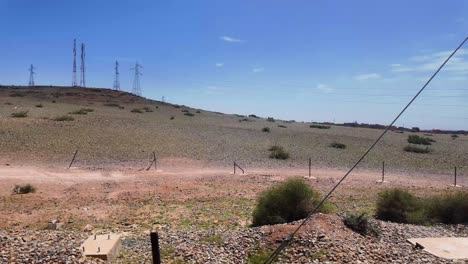 Train-travelling-in-Morocco,-arid-land-and-high-voltage-power-lines