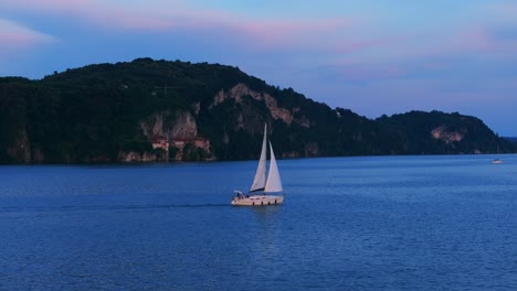 Sailboat-sailing-at-sunset-on-Maggiore-lake-surrounded-by-picturesque-hillside-town-in-Italy