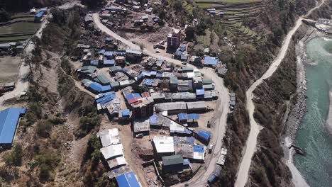 Vista-Aérea-Del-Pintoresco-Paisaje-De-Un-Pueblo-De-Montaña-En-Un-Terreno-Accidentado,-Un-Pintoresco-Pueblo-De-Montaña-Con-Edificios-Con-Techos-Azules-Ubicado-En-Medio-De-Campos-En-Terrazas-Y-Un-Río-Sinuoso